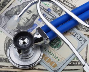 USD bank notes with a stethoscope and calculator showing the high cost of health care
